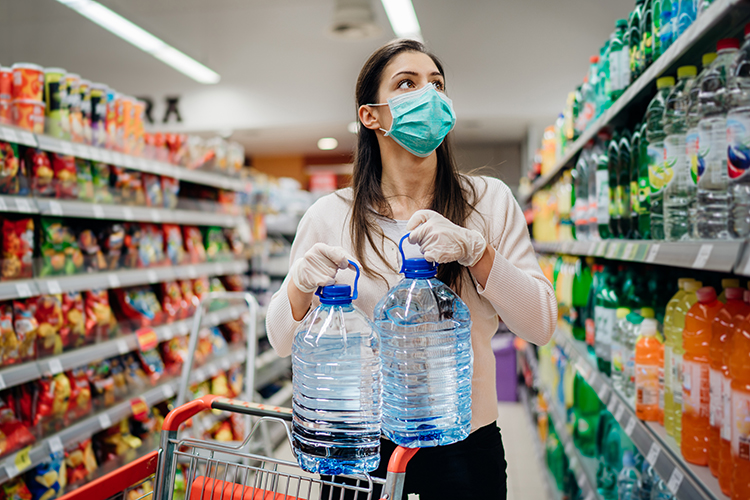 Woman wearing face mask buying bottled water in supermarket/drug